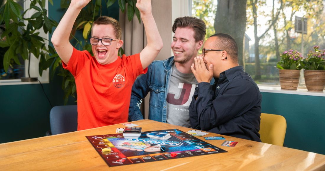 Een begeleider met 2 gehandicapten jongens zijn een bordspel aan het spelen.